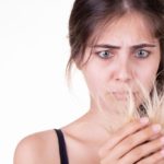 Young adult woman looking desperately at her worn hair, studio shoot